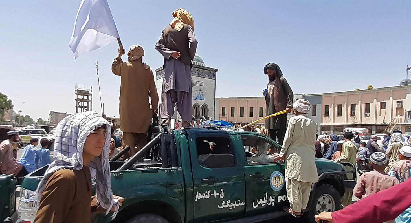 Taliban fighters stand over a damaged police vehicle along the roadside in Kandahar on August 13, 2021