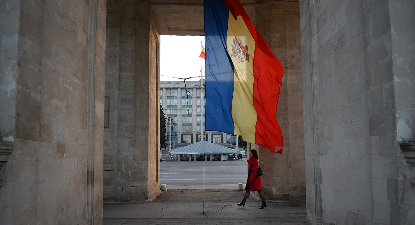 A woman walks under the Triumph Arch next to Moldovan flag 
