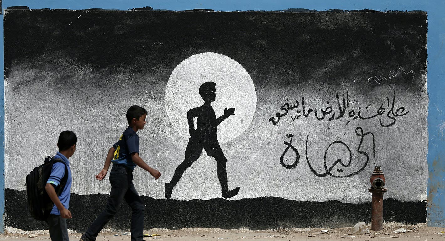 Two Palestinian schoolboys walk past a graffiti painted on a wall of a UN school in Gaza
